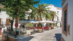 A narrow street with outdoor seating, palm trees, and white buildings with red shutters. - Stunning home in El Gastor (El Gastor)