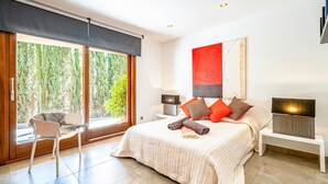 A modern bedroom with a large bed, a chair, a desk, and a window with a view of trees. - Stunning home in Mancor de la Vall (Mancor de la Vall)
