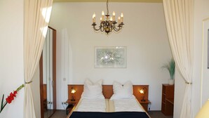 Camera d'albergo con un letto matrimoniale, un lampadario, un quadro incorniciato, un comodino con una lampada e una pianta in vaso.