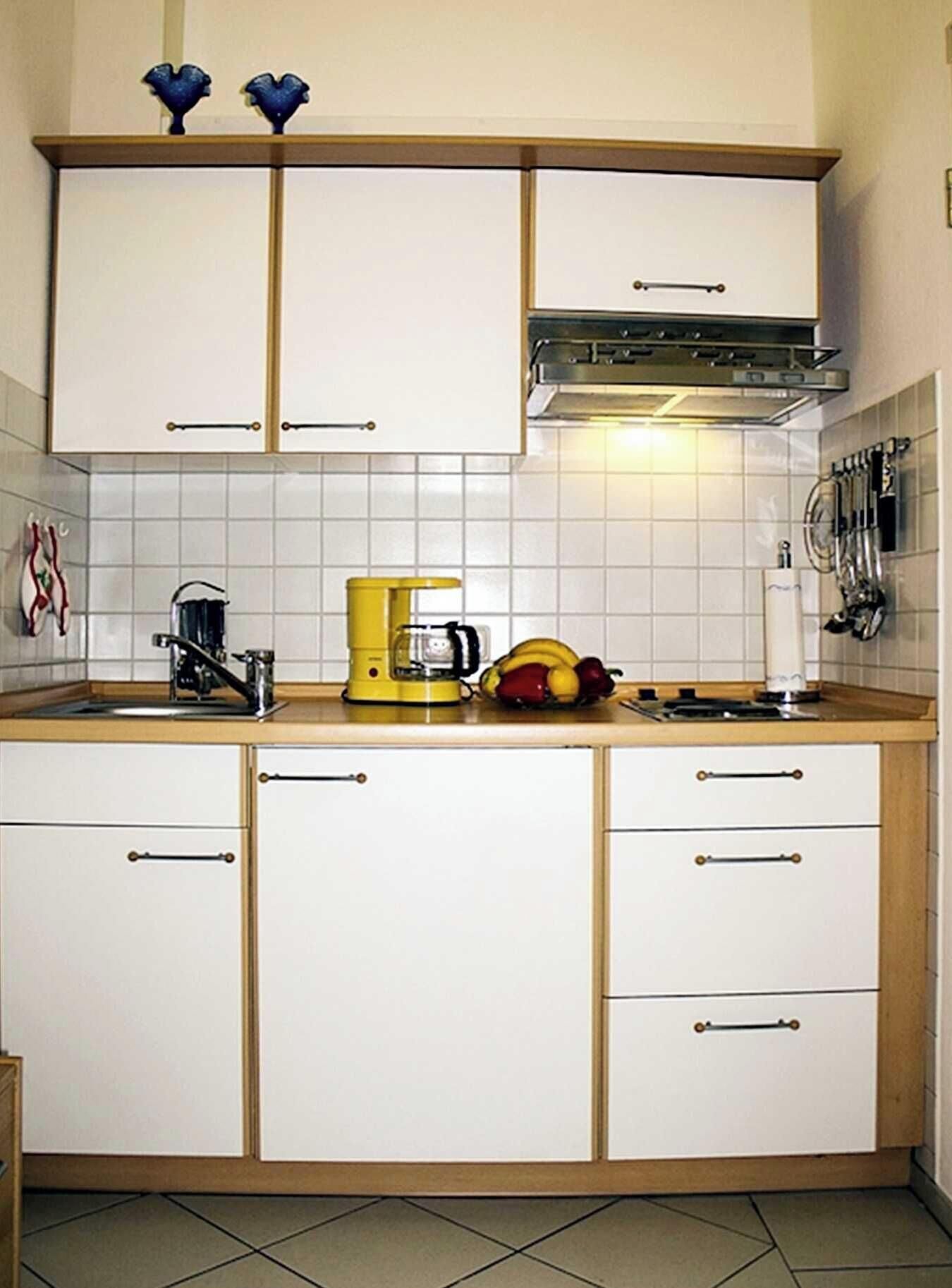 A kitchen with white cabinets, a yellow coffee maker, and a fruit bowl on the counter.