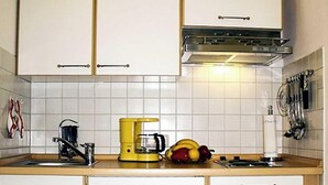Una cucina con mobili bianchi, una macchina da caffè gialla e una ciotola di frutta sul piano di lavoro.