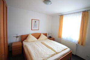Een slaapkamer met een enkel bed, houten hoofdbord, nachtkastjes, een ingelijst schilderij aan de muur en een raam met gordijnen.