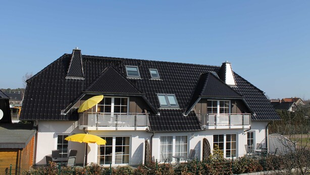 Une maison à deux étages, avec un toit sombre, de nombreuses fenêtres et un balcon.