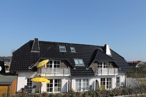 Een tweelaags huis met een donker dak, meerdere ramen en een balkon.