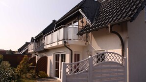 Une maison à deux étages avec un balcon, une entrée sécurisée par un portail et une allée pavée.