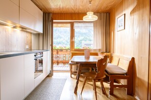 A modern kitchen with a built-in oven, a dining table with chairs, and a view of a forested area through a large window.