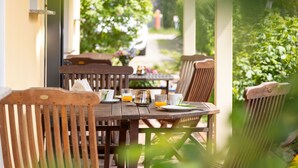 A wooden table with chairs, a glass of orange juice, and a cup on a balcony overlooking a garden. - Vacation home 04 and terrace - Holiday apartments with terrace in Sellin for (Sellin)