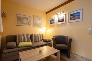 Un salon comprenant un canapé, un fauteuil, une table basse et des tableaux accrochés au mur.