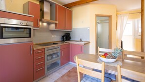 A compact kitchen with a built-in oven, a coffee maker, and a dining table with a fruit bowl. - Vacation home 04 and terrace - Holiday apartments with terrace in Sellin for (Sellin)