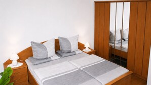 A neatly made bed with a grey and white striped bedspread, two bedside lamps, and a wooden wardrobe with a mirror. - Apartment Ivan (2nd floor) - Ivan Apartments - Property 26001 (Rostock)
