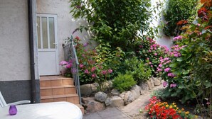 A patio with a white table and chairs, a stone pathway, and a variety of flowering plants. - Apartment Ivan (2nd floor) - Ivan Apartments - Property 26001 (Rostock)