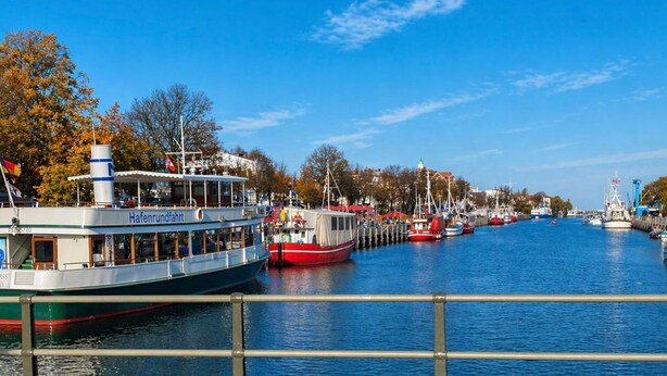 A river with boats docked along the banks, a wooden walkway, and trees with autumn foliage. - Apartment Ivan (2nd floor) - Ivan Apartments - Property 26001 (Rostock)
