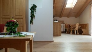 A wooden dining table with a vase of flowers, a wooden bench, and a high ceiling with a skylight. - Apartment Blauberg - Böcklhof, Kreuth-Brunnbichl (Kreuth)