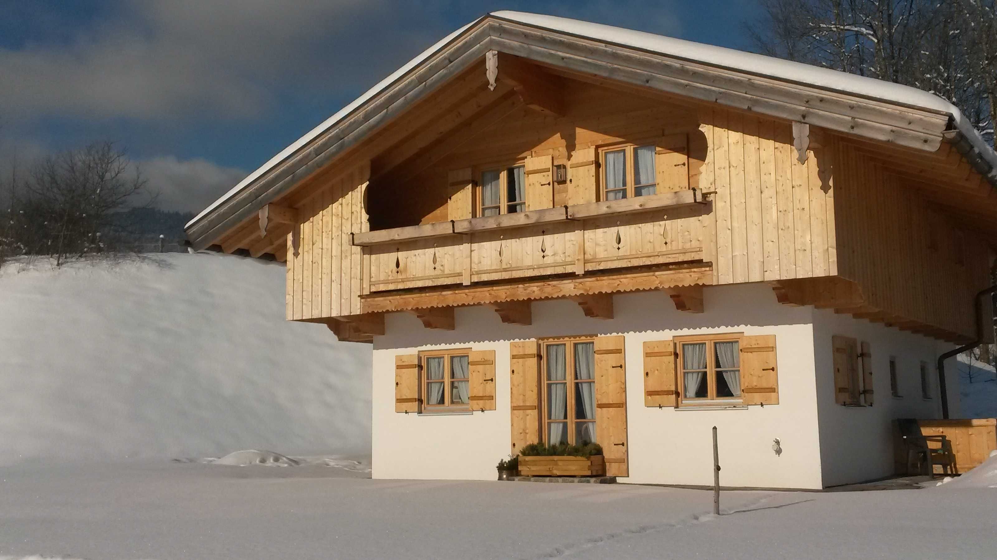 A wooden chalet with a balcony, large windows, and a snow-covered ground.