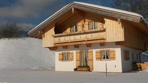 Un chalet en bois doté d’un balcon, de grandes fenêtres et d’un terrain enneigé.