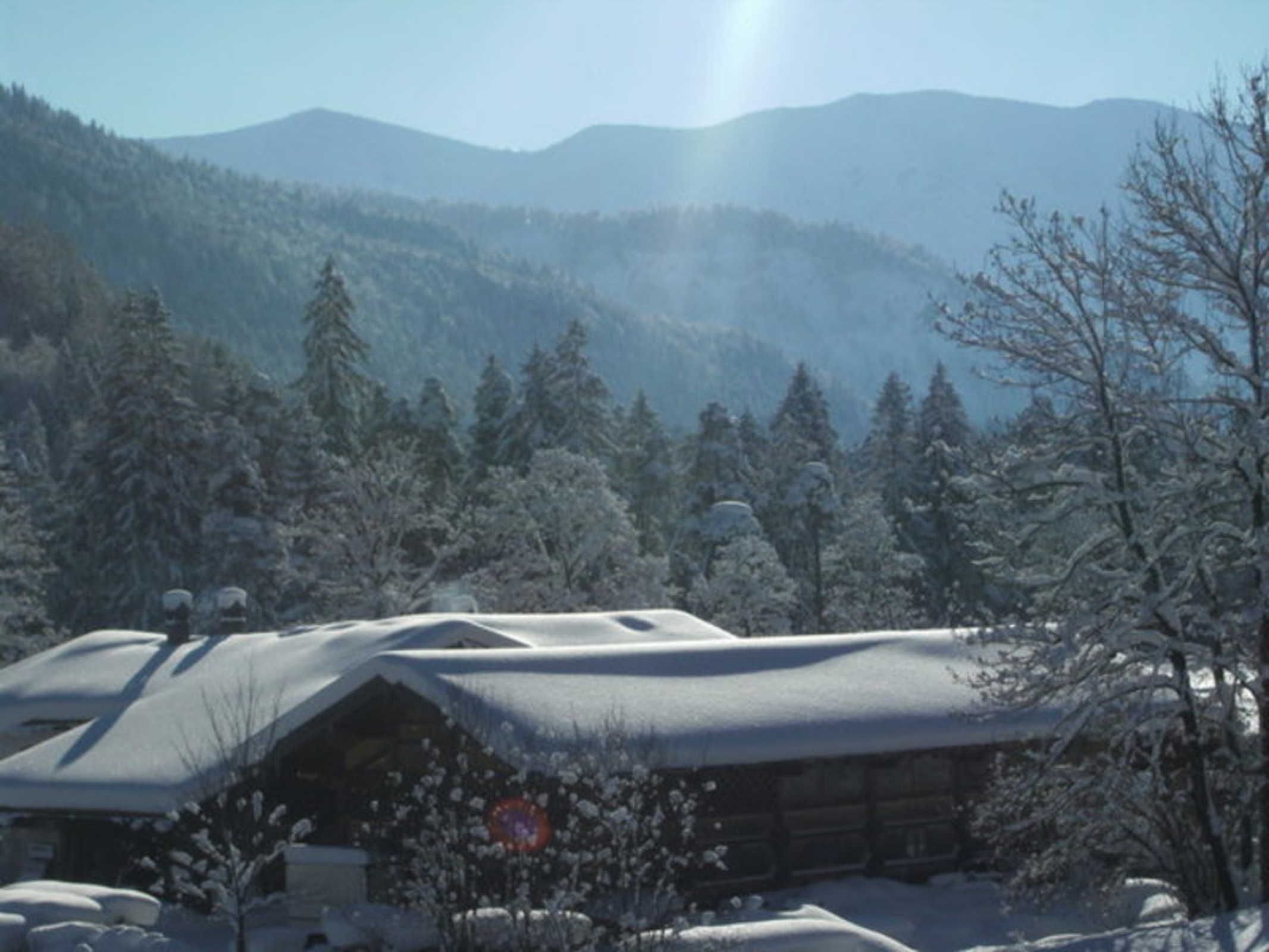 A cabin with a snow-covered roof, surrounded by trees and mountains.