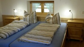 Een tweepersoonsbed met gestreept beddengoed, twee nachtkastjes, een raam met gordijnen en een stopcontact.