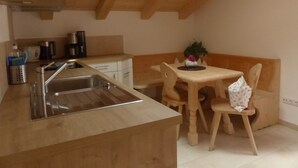 A kitchen with a wooden countertop, a sink, and a dining area with a table and chairs. - Apartment Blauberg - Böcklhof, Kreuth-Brunnbichl (Kreuth)