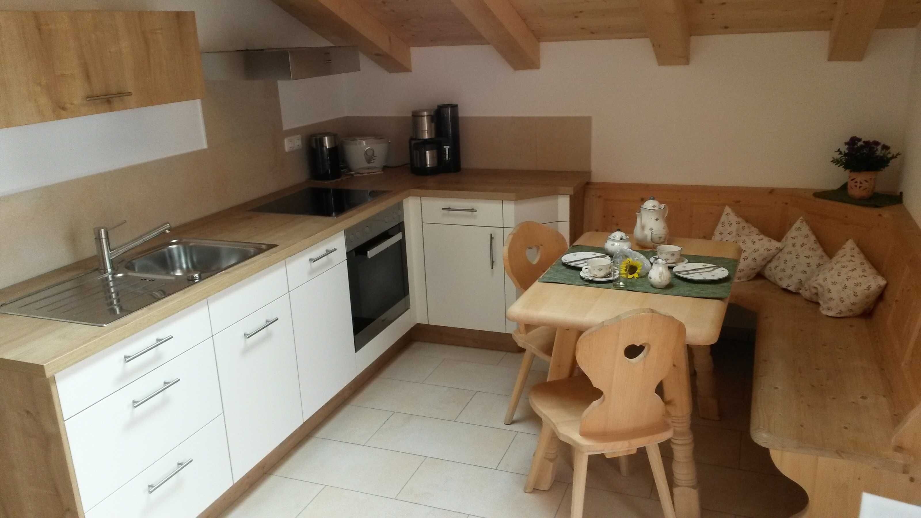 Een compacte keuken met witte kastjes, een spoelbak, een fornuis en een eethoek met een tafel voor twee personen.