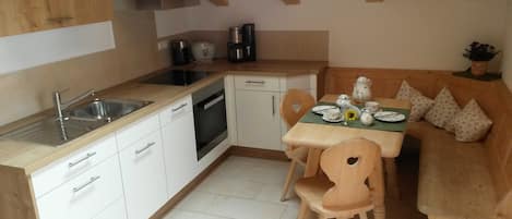 Een compacte keuken met witte kastjes, een spoelbak, een fornuis en een eethoek met een tafel voor twee personen.