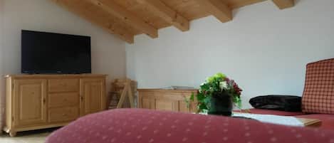 Una habitación con techo de madera, un televisor sobre un mueble, un sofá rojo y una pequeña mesa con un florero.