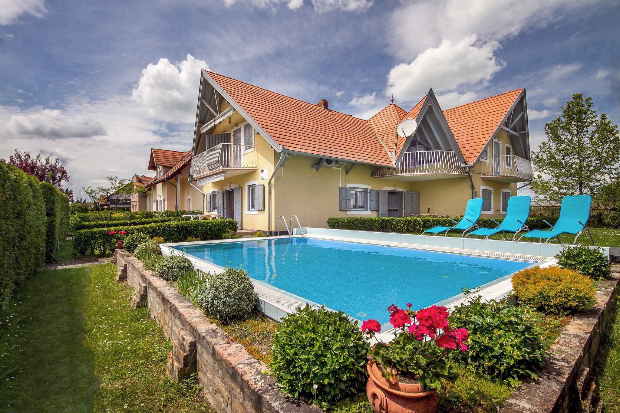 A two-story house with a swimming pool, blue lounge chairs, and a well-maintained garden.