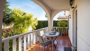 Un porxo cobert amb una taula rodona i cadires, envoltat de plantes en testos i una barana blanca.