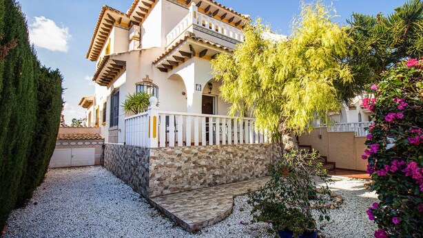 Una casa de dues plantes amb façana de pedra, un balcó i un camí d'accés de grava.