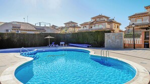 Una piscina de vora corbada, envoltada per una terrassa pavimentada. Hi ha gandules i un petit parasol a prop de la piscina.