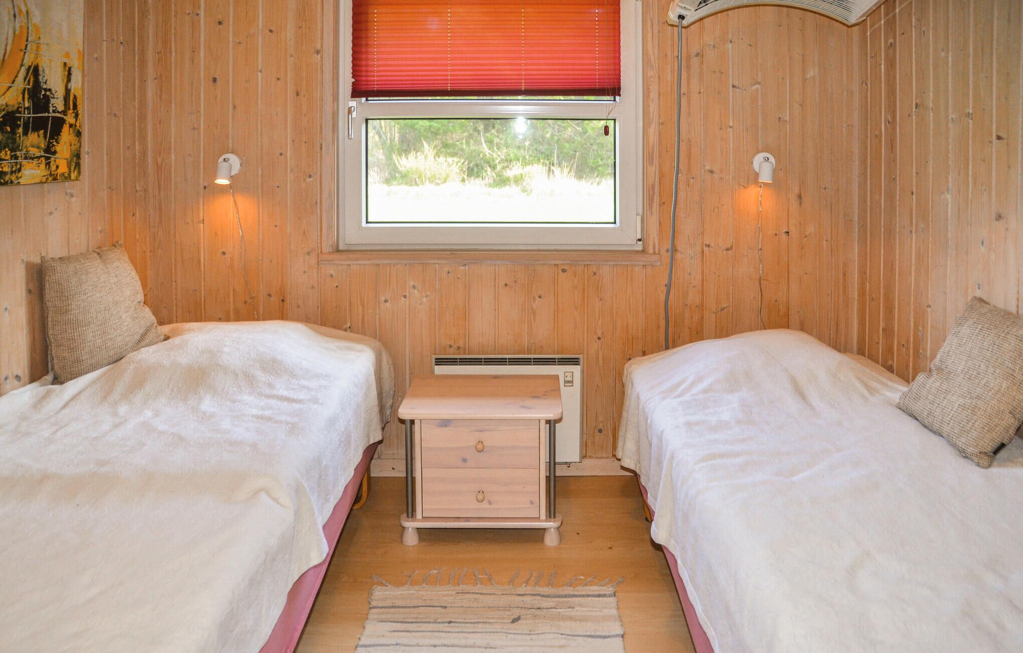 A room with two beds, a small table, a window with a view, and wooden walls.