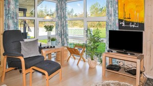 Ein Wohnzimmer mit Fernseher, zwei Sesseln, einem kleinen Tisch und einer Pflanze.