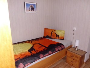 A bed with a colorful blanket, a pillow with a giraffe design, a bedside lamp, and a small wooden nightstand.