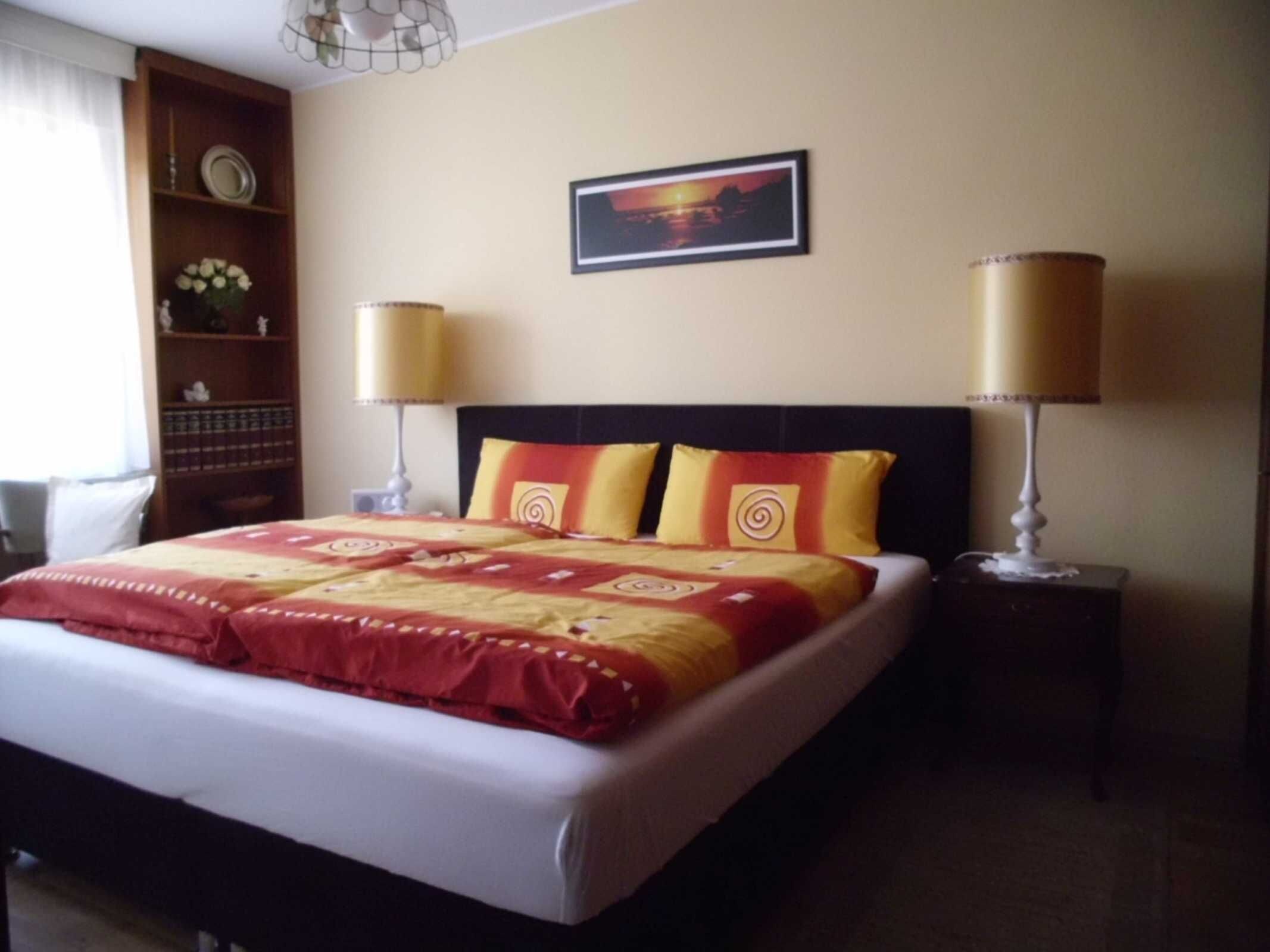 Ein Hotelzimmer mit einem Bett, zwei Nachttischlampen, einem Bild an der Wand und einem Regal mit Dekoration.