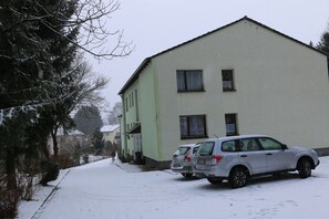 Un edificio de dos pisos con techo plano, un coche estacionado y nieve en el suelo.