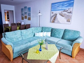 Uma sala de estar com um sofá seccional, uma mesinha com um vaso e obras de arte nas paredes.