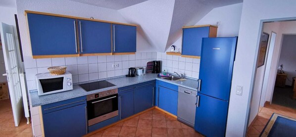 Uma cozinha compacta com armários azuis, micro-ondas, torradeira e máquina de lavar louça.