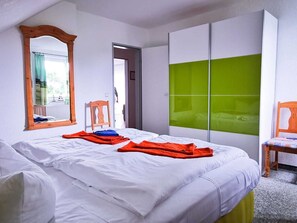 Quarto de hotel com duas camas, um espelho grande, um guarda-roupa com painéis verdes e uma cadeira.