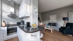 A modern kitchen with white cabinets, a built-in oven, and a dark countertop. There is a bowl of fruit on the counter, a coffee maker, and a clock on the wall. - Apartment 01 - "Villa Minerva" Apartment 01 (Kühlungsborn)