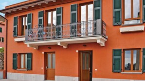 Um edifício de dois andares com venezianas verdes, uma varanda com grades de metal ornamentadas e uma base branca.