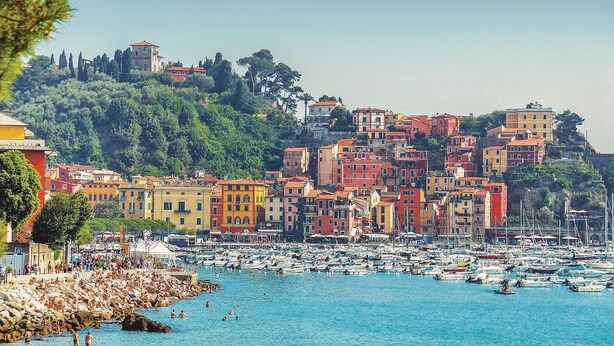 Uma cidade costeira com edifícios coloridos, uma marina com muitos barcos e pessoas aproveitando a orla.