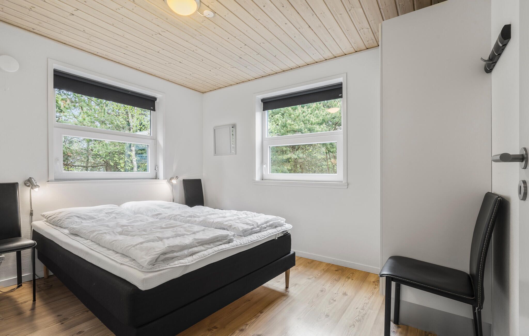 Ein Schlafzimmer mit einem Bett, zwei Fenstern, einem Sessel und einer Tür.