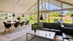 A spacious room with a large window, a dining area with a table and chairs, a sofa, and a coffee table. - Nice home in Væggerløse with sauna (Væggerløse)