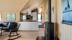 A cozy cabin interior with a kitchen, a living area with a sofa and a rocking chair, and a large poster on the wall. - Nice home in Væggerløse with sauna (Væggerløse)
