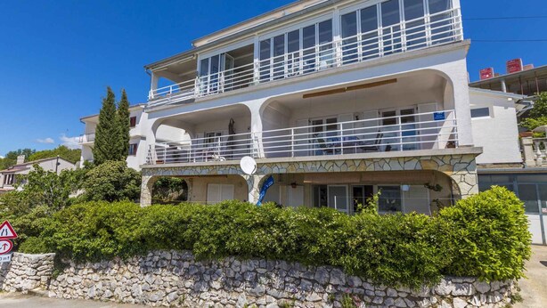 A two-story building with a balcony on the upper floor, a stone wall in front, and a clear blue sky. - Holiday apartment with sea view (Dramalj)