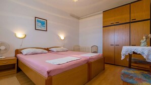 A bedroom with two beds, a wooden wardrobe, a crib, a table with a lace tablecloth, and a wall-mounted light fixture. - Holiday apartment with sea view (Dramalj)