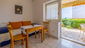 A room with a sofa, a table, and chairs, a window with a view of a garden, and a framed picture on the wall. - Holiday apartment with sea view (Dramalj)