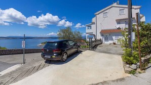 A black car parked in front of a white building with a red-tiled roof, near a body of water and a clear blue sky. - Holiday apartment with sea view (Dramalj)