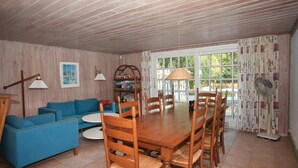 A dining area with a wooden table and chairs, a blue sofa, and a bookshelf. - 3 bedroom awesome home in Skælskør (Skælskør)