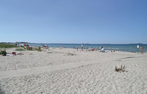 Une plage de sable où des gens se prélassent au soleil et se baignent.