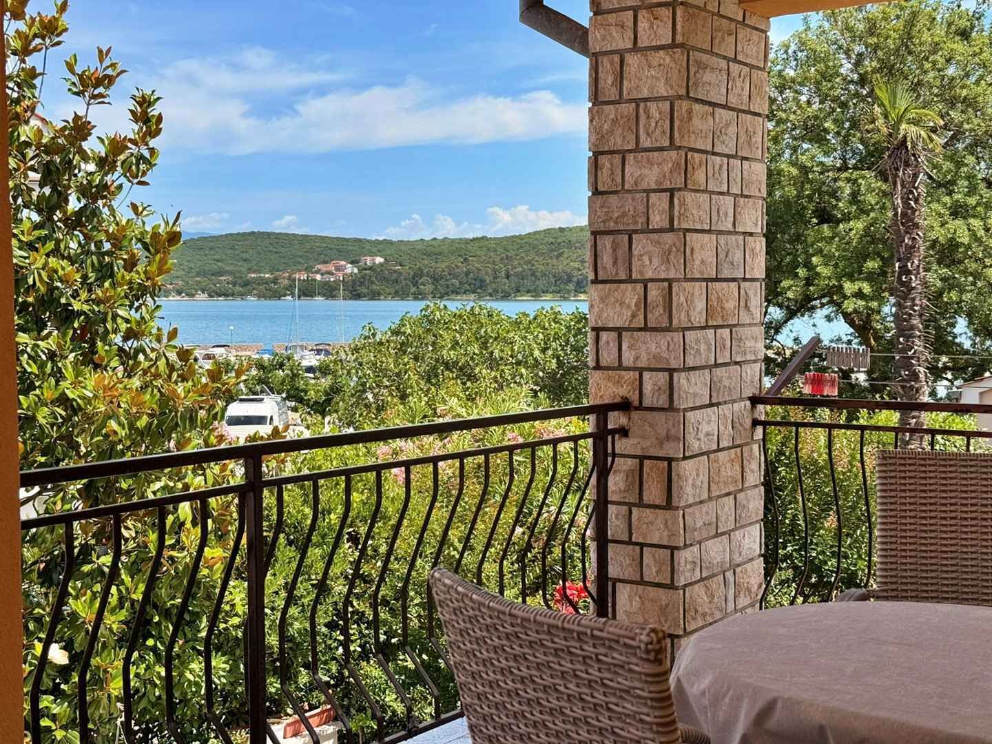 Un balcón con vistas a un lago, rodeado de vegetación y un pilar de piedra.